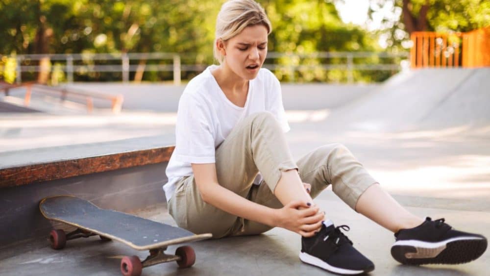 upset-skater-girl-holding-her-painful-leg-with-skateboard-near-while-spending-time-skatepark