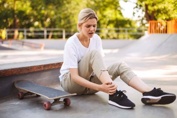 upset-skater-girl-holding-her-painful-leg-with-skateboard-near-while-spending-time-skatepark